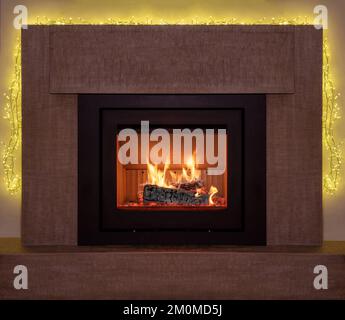 Bonfire, burning fireplace, Christmas lights decoration. Energy wood logs fireside and marble stone frame, front view. Stock Photo