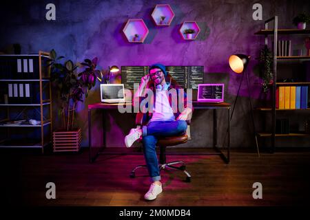 Photo of smiling positive guy dressed glasses hat working late night shift indoors workstation workshop home Stock Photo