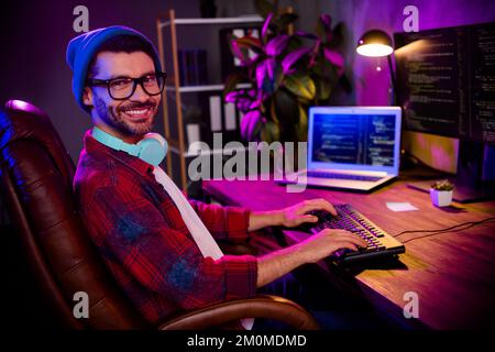Photo of happy smiling programmer wear spectacles hat creating software modern device indoors workplace workshop home Stock Photo