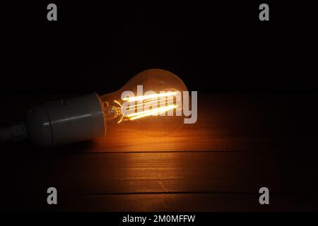 burning light bulb on wood surface and black background Stock Photo