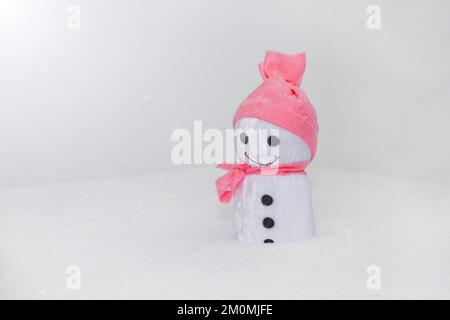 smowman standing on snow. handmade toy with pink fabric hat and white snowflakes- standing close up Stock Photo