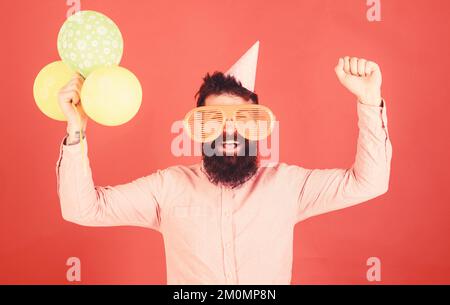 Hipster in giant sunglasses celebrating birthday. Guy in party hat celebrates holiday. Celebration concept. Man with beard and mustache on happy face Stock Photo