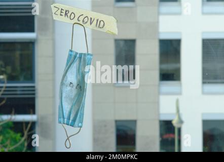 Zero covid sign and old surgical mask on window, office buildings in the back Stock Photo