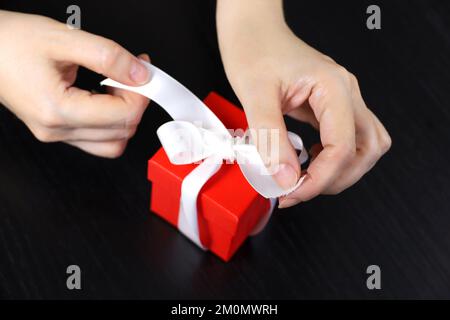 Female hands with red gift box on dark wooden table. Concept of Christmas holiday, romantic surprise Stock Photo