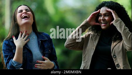 Two candid women laughing and smiling together outside, real life laugh Stock Photo