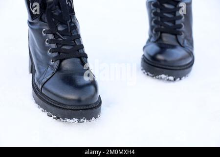 Female feet in black leather lace-up boots on a snow. Woman walking on winter street, warm footwear for cold weather Stock Photo