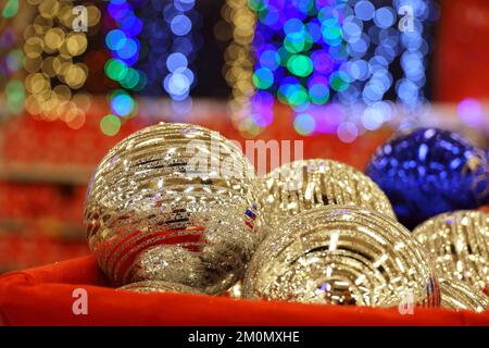 Christmas toys, golden and blue balls in red basket on blurred festive lights background. New Year decorations in a store Stock Photo