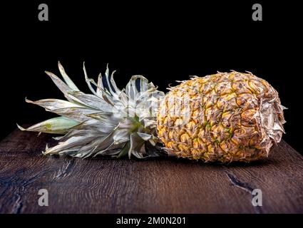 Ripe pineapple lies on a wooden table against a black background. Copy space. Stock Photo