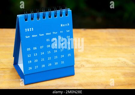 March 2023 blue desk calendar on wooden table background with customizable space for text. Stock Photo