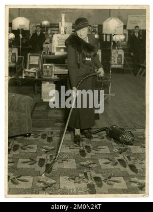 Original 1930's era press release from an electrical household goods showroom, maybe in-store demonstration in a department store, by smartly dressed woman demonstrator -  staff or customer, demonstrating using a vacuum cleaner in U.K. furniture shop showroom, early labour saving housework device, UK circa.1933. Stock Photo
