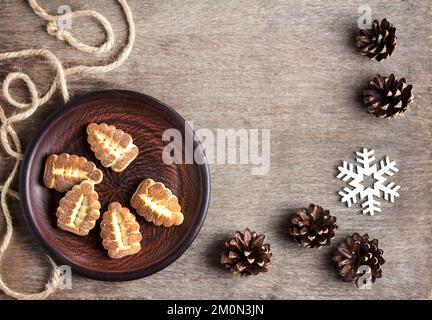 Rustic winter composition with shortbread cookies on a brown clay plate and pinecones on a wooden background. Flat lay, top view Stock Photo