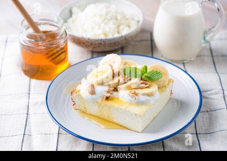 Cheese cake, cottage cheese casserole Zapekanka served with banana slices, chopped nuts, honey and greek yogurt. Healthy breakfast food rich in Calciu Stock Photo