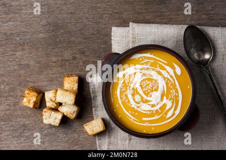 Pumpkin soup with cream and sesame seeds in brown ceramic bowl on wooden background. Flat lay, top view. Stock Photo