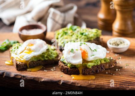 Rye toast with mashed avocado and poached egg on wooden board, closeup view. Healthy breakfast avocado toast Stock Photo
