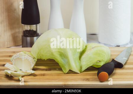 Cabbage leaves on a cutting board with a knife - kitchen table in the background Stock Photo