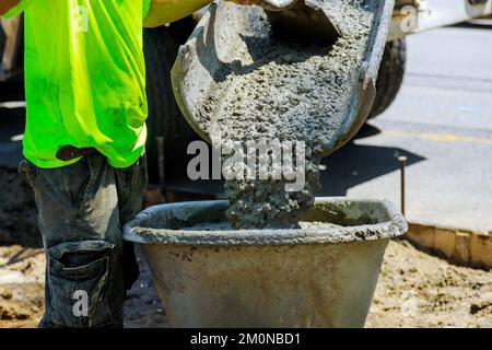 In construction site concrete mixer truck is pouring wet cement into wheelbarrow Stock Photo