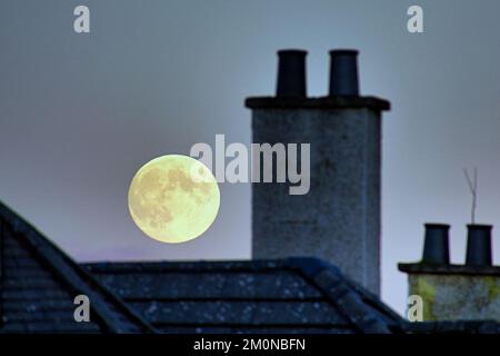 Glasgow, Scotland, UK 7th December, 2022. UK Weather:  Freezing temperatures aptly saw the  Cold Moon rise tonight, the last full moon of 2022. The rooftops if the suburb of knightswood and the corby step tower of the church at knightswood cross. Credit Gerard Ferry/Alamy Live News Stock Photo