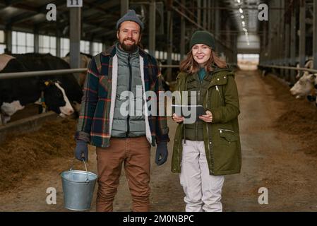 Portrait of couple of farmers smiling at camera standing in barn, they working on big dairy farm Stock Photo