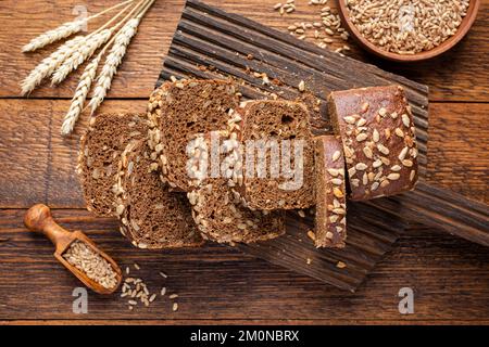 Whole grain rye bread with seeds cut into bread slices on wooden board, top view Stock Photo