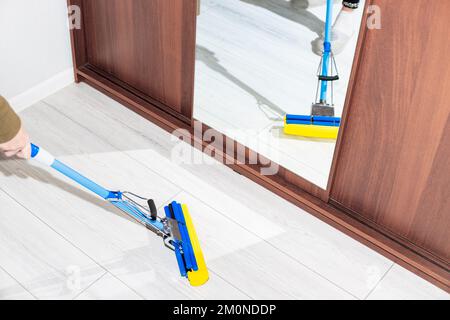 A woman mops the floor in the room, reflected in the mirrored closet door. Cleaning in the house. Stock Photo