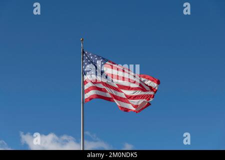 A large American flag blows in the wind against a bright blue sky. Stock Photo