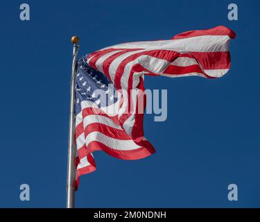 A large American flag blows in the wind against a bright blue sky. Stock Photo