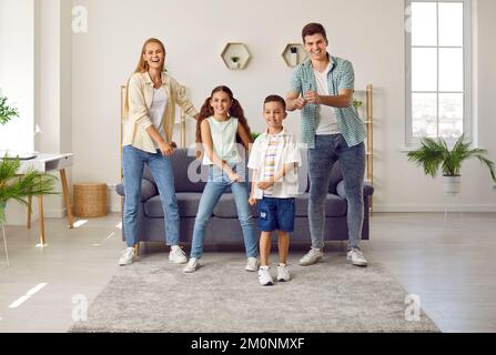 Happy family of four is having fun dancing to music in living room of bright apartment. Stock Photo