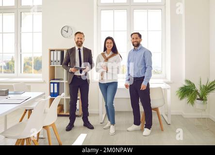 Portrait of three joyful business team colleagues posing together standing in row in office. Stock Photo