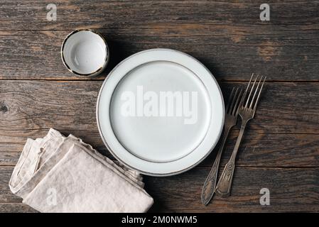 Empty plate, vintage silverware and linen kitchen textile on old wooden table. Rustic table setting, top view, copy space for text or design elements Stock Photo