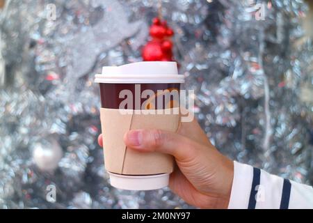 Hand Holding Takeaway Coffee Cup with Blurry Glittering Christmas Tree in Background Stock Photo