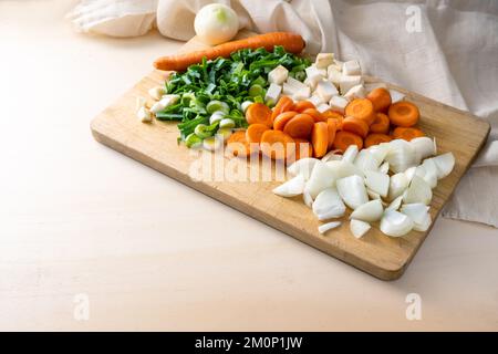 Chopped vegetables, ingredients for soups or sauces with carrots, onions, leeks and celery on a wooden cutting board in the kitchen, cooking concept, Stock Photo
