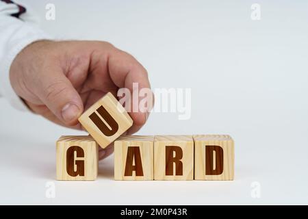 Business concept. On a white surface, a man stacks cubes with the inscription - Guard Stock Photo