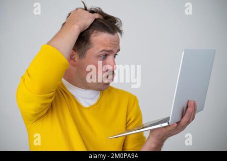 Thinking young man standing with laptop looking on screen with confused face Stock Photo