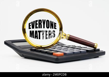 Finance and business concept. On a white background lies a calculator and a magnifying glass with the inscription - Everyone Matters Stock Photo