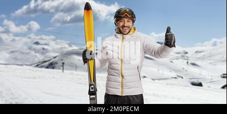 Smiling young man with skiiing equipment posing on a mountain and gesturing thumbs Stock Photo