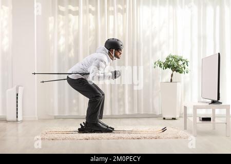 Profile shot of a man skiing at home in a living room in front of  tv Stock Photo