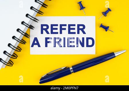 Business and finance concept. On a yellow background lies a notebook, a pen and a business card with the inscription - Refer a friend Stock Photo
