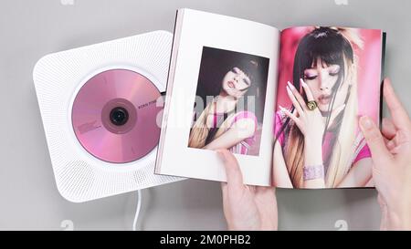 Fan hands holding BlackPink BORN PINK 2nd Album photobook with Lisa on grey. Pink music CD in player. South Korean girl group BlackPink. Space for tex Stock Photo