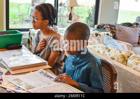two kids , boy and girl sitting at the kitchen table doing homework. Stock Photo