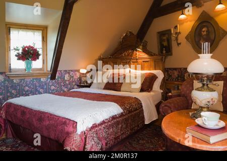 Large bed with crimson colored silk bedspread in master bedroom inside 1977 built replica of old 1800s Canadiana cottage style log cabin. Stock Photo