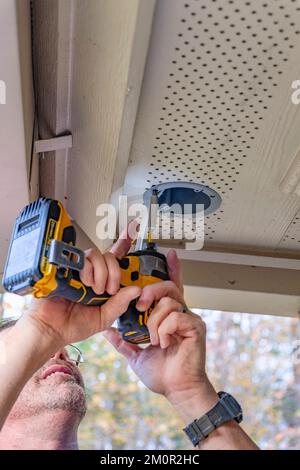 Electrician or handyman at work installing outside security lights using a battery powered electric drill or screwdriver to make the installation. Stock Photo