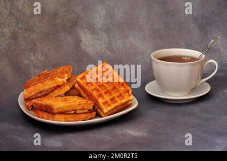 A plate with several Viennese waffles and a cup of hot tea on a gray abstract background. Close-up. Stock Photo