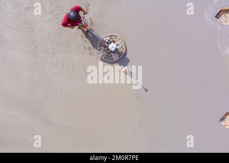 Worker polishing and leveling cement screed floor on construction site Stock Photo