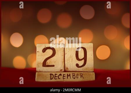 December 29 vintage wooden block calendar on red fabric, festive bokeh lights background greeting card celebrating holidays, birthday, save the date f Stock Photo