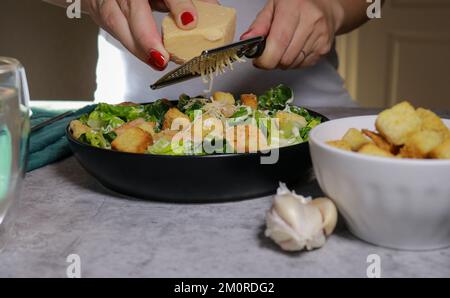woman grating parmesan cheese on top of Caesar salad with shrimp Stock Photo