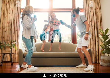 Young happy mother and father singing and dancing with their little daughters in the lounge at home. Cheerful little siblings playing guitar and Stock Photo