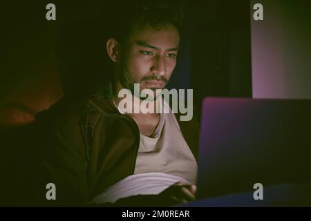 Indian man hallucinating and feeling paranoid while using his laptop in his messy bedroom at home. Young man feeling stressed and scared Stock Photo