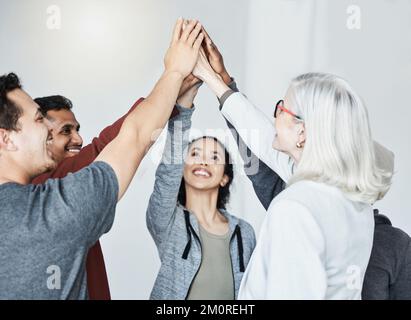 Diverse group of five businesspeople smiling giving each other a high five in a meeting in an office at work. Happy women and men joining their hands Stock Photo