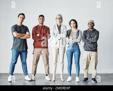 Portrait of team of focused united young business people folding arms. Diverse mixed race group of men and women standing in row in office, looking Stock Photo