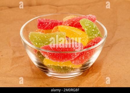 Several sweet marmalade candies in a glass plate on kraft paper, macro. Stock Photo